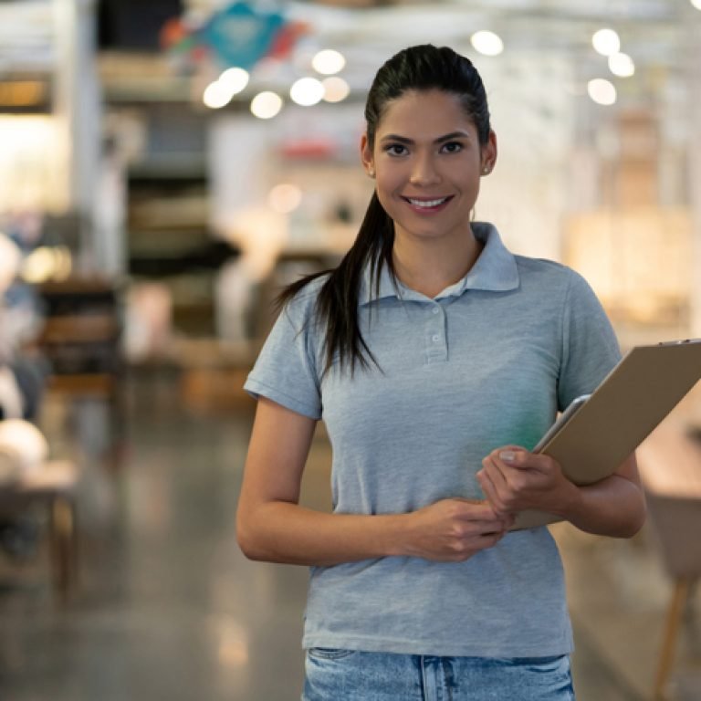Young saleswoman at a furniture store holding a clipboard smiling at camera very cheerfully